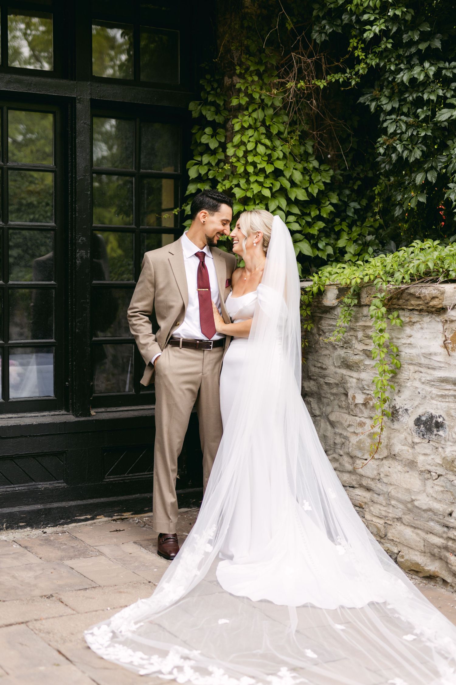 Newlyweds share intimate moments against a stone wall backdrop with flowing white wedding dress.