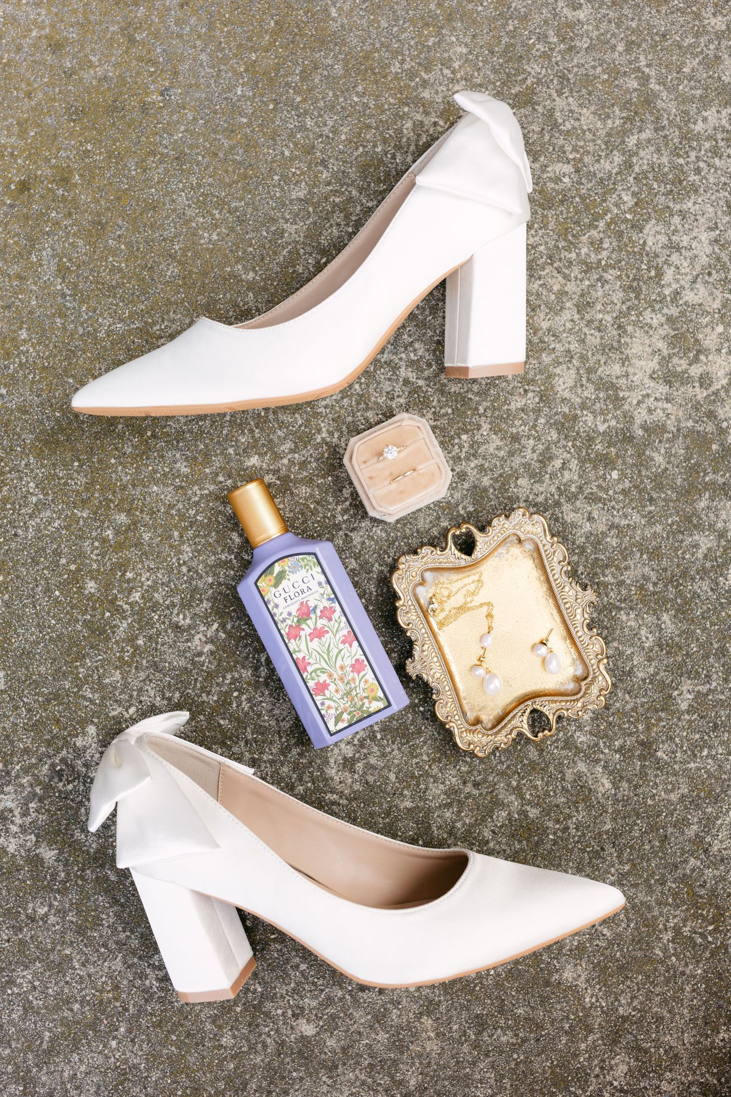 White bridal heels and vintage accessories arranged on textured concrete surface.