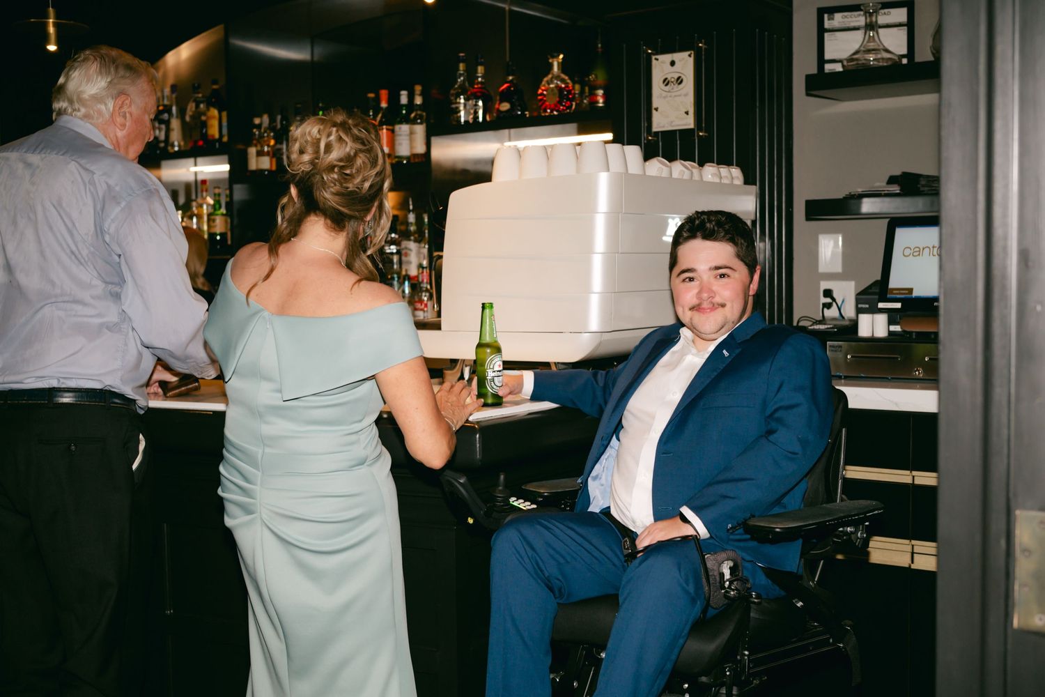 Wedding guests socializing at indoor bar area during reception.