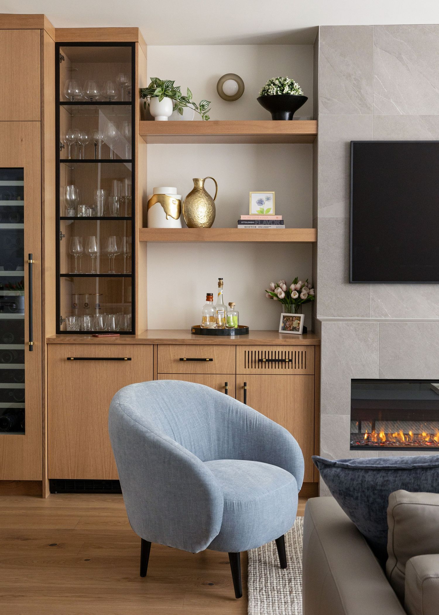 Contemporary living space with glass-front storage, floating shelves, and blue accent chair.