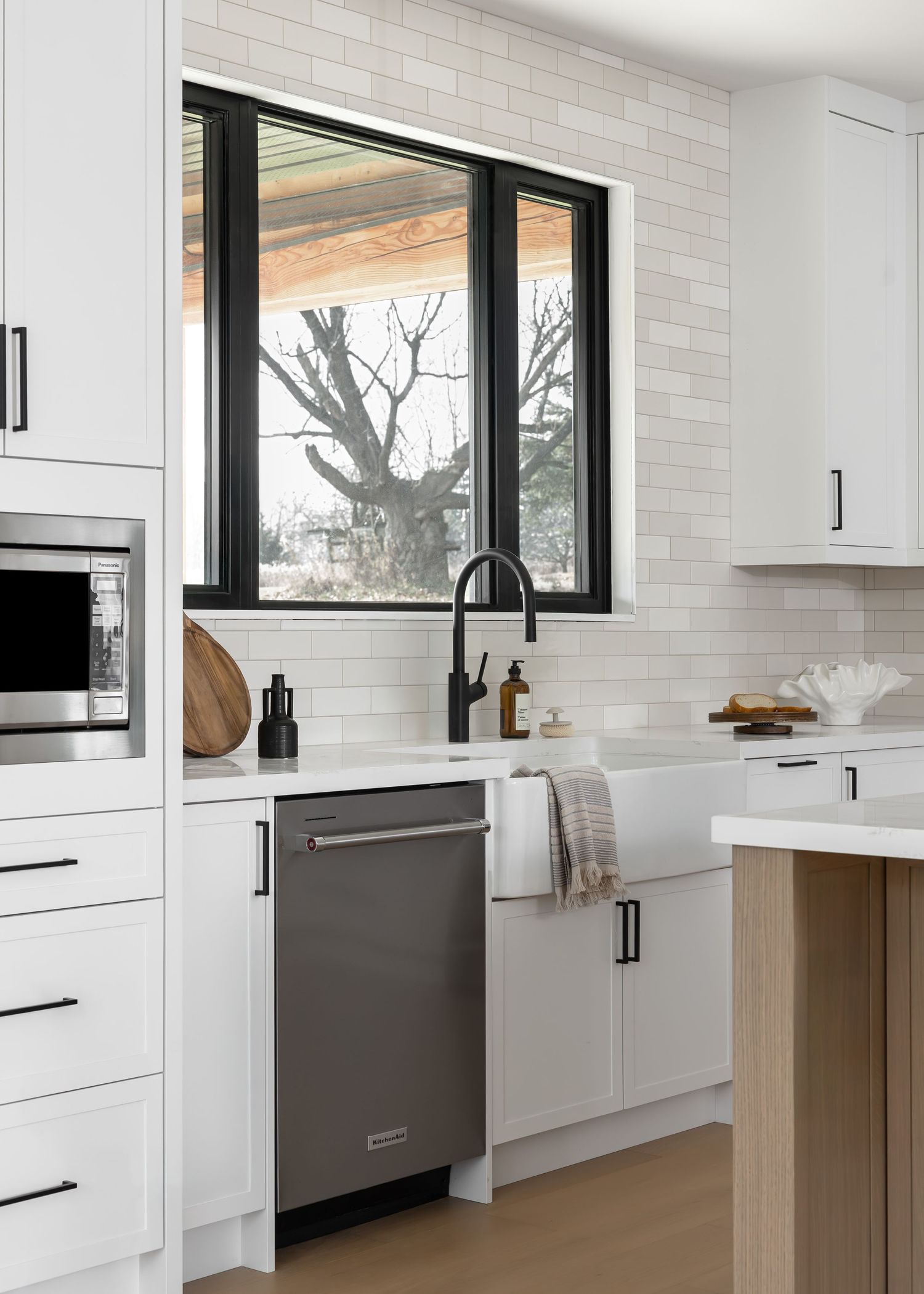 Contemporary kitchen featuring white cabinets, black-framed windows, and stainless steel appliances.