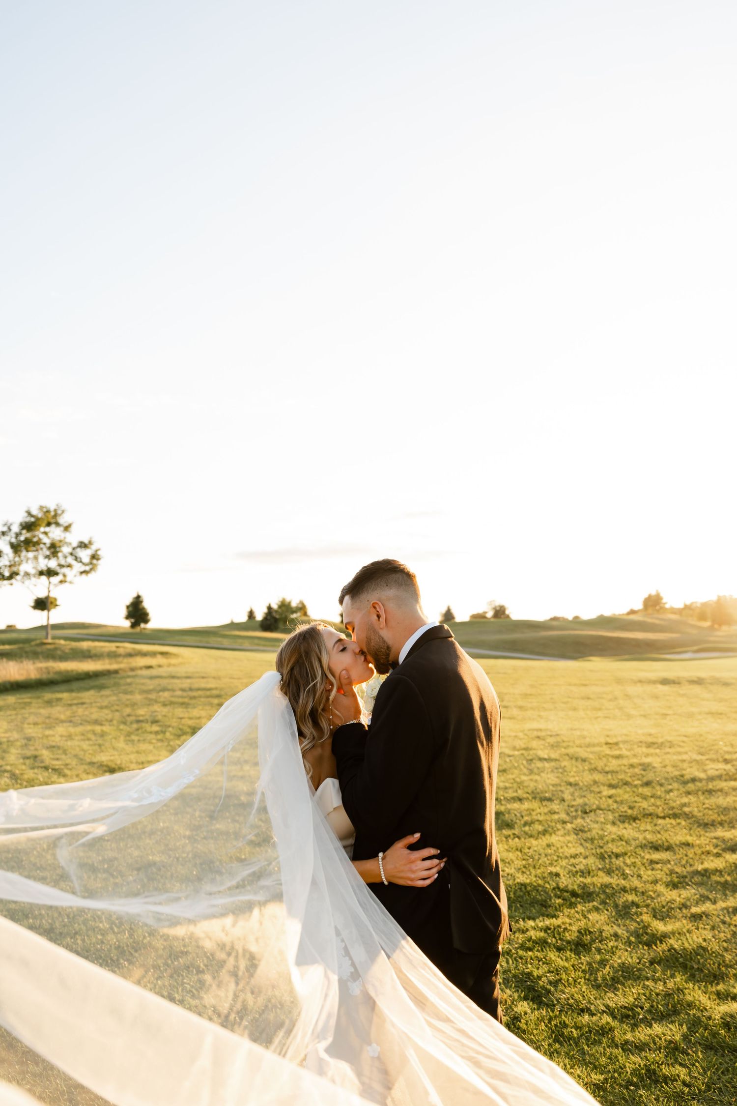 Wedding couple shares an intimate moment on a golf course during sunset.