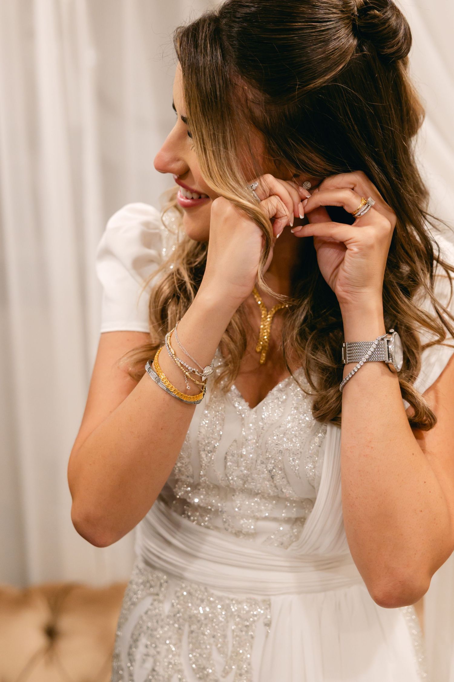 Putting on jewelry and accessories while wearing a beaded white wedding gown.
