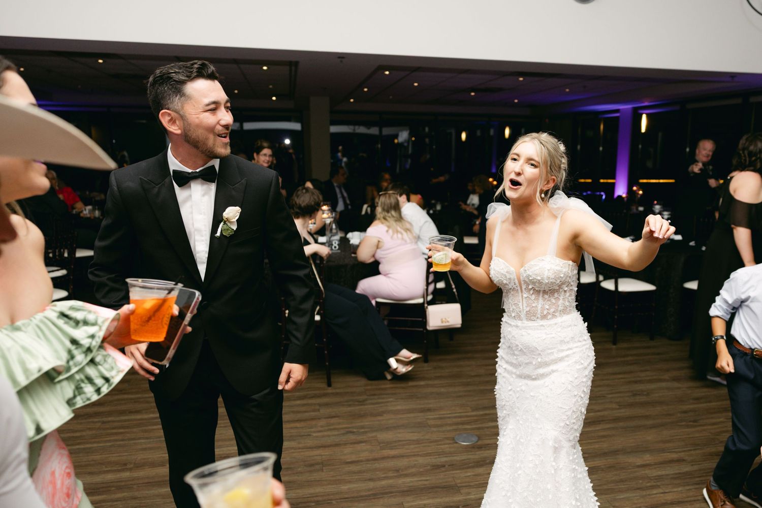 Wedding guests dance and celebrate on a dark dance floor with purple lighting.