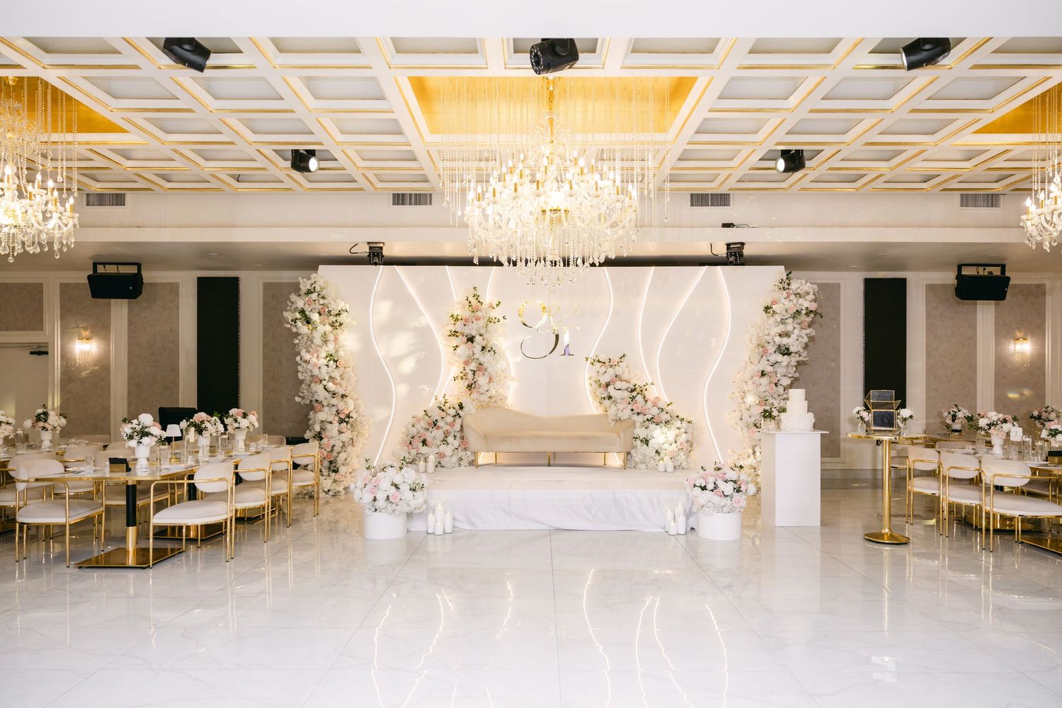 Spacious white wedding venue featuring dramatic chandeliers and modern architectural details.