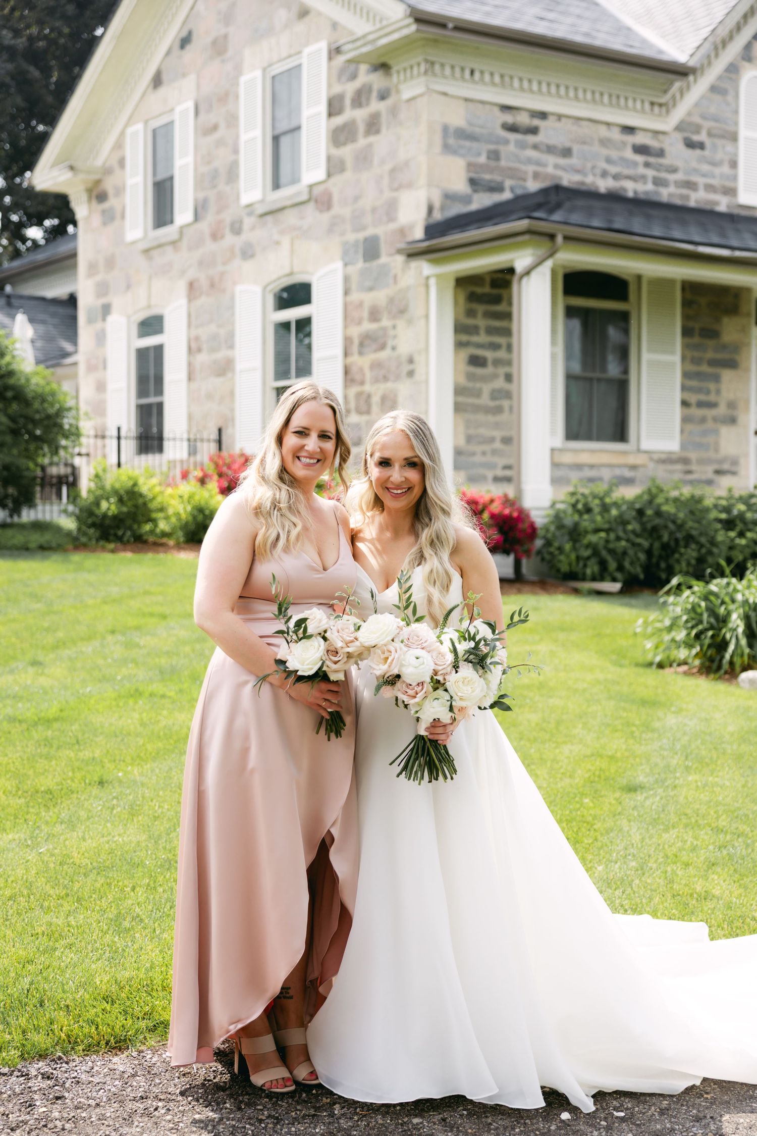 Bridal party members share joyful moment together outside stone building.