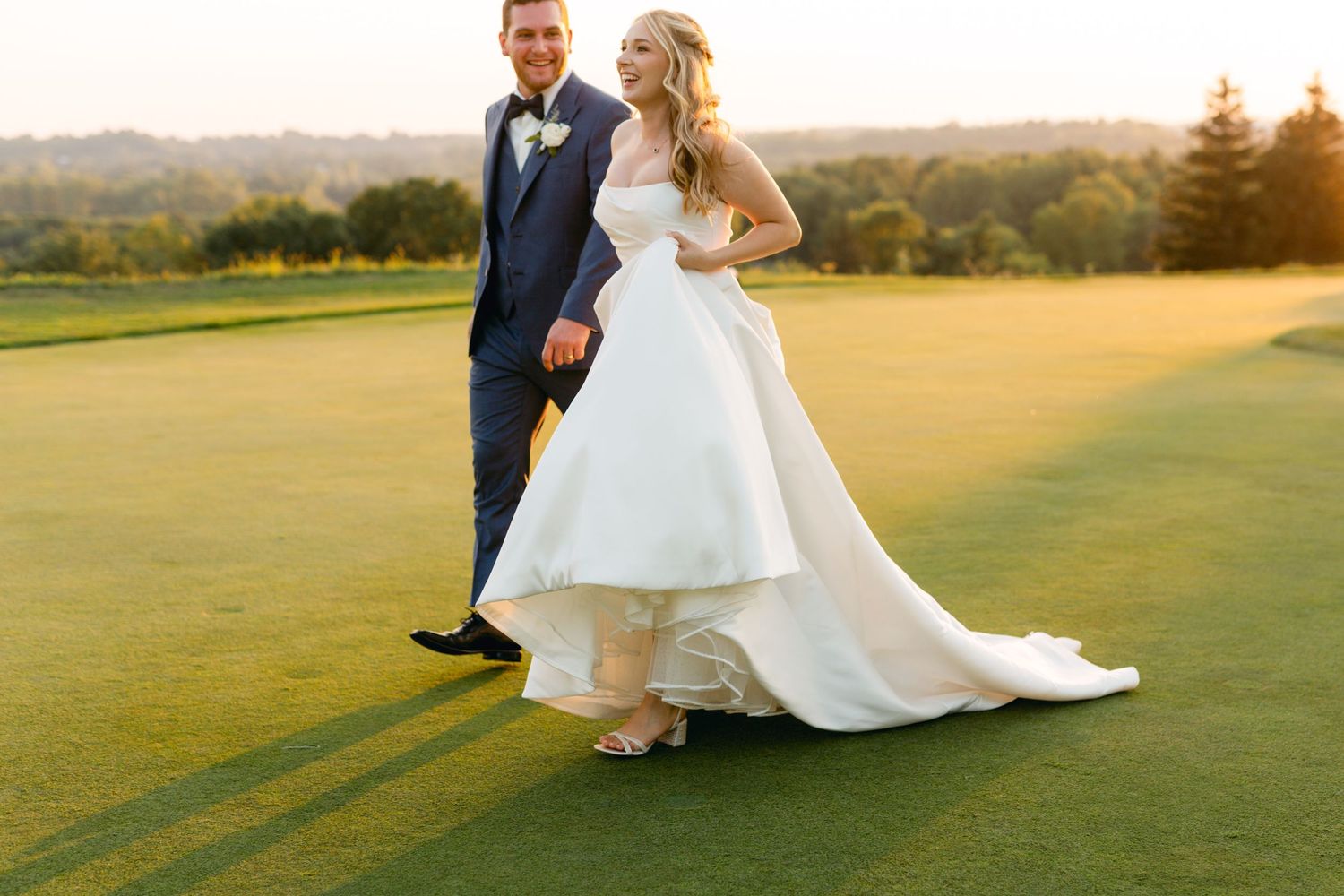 Elegant couple walks across a manicured golf course during their wedding photoshoot.