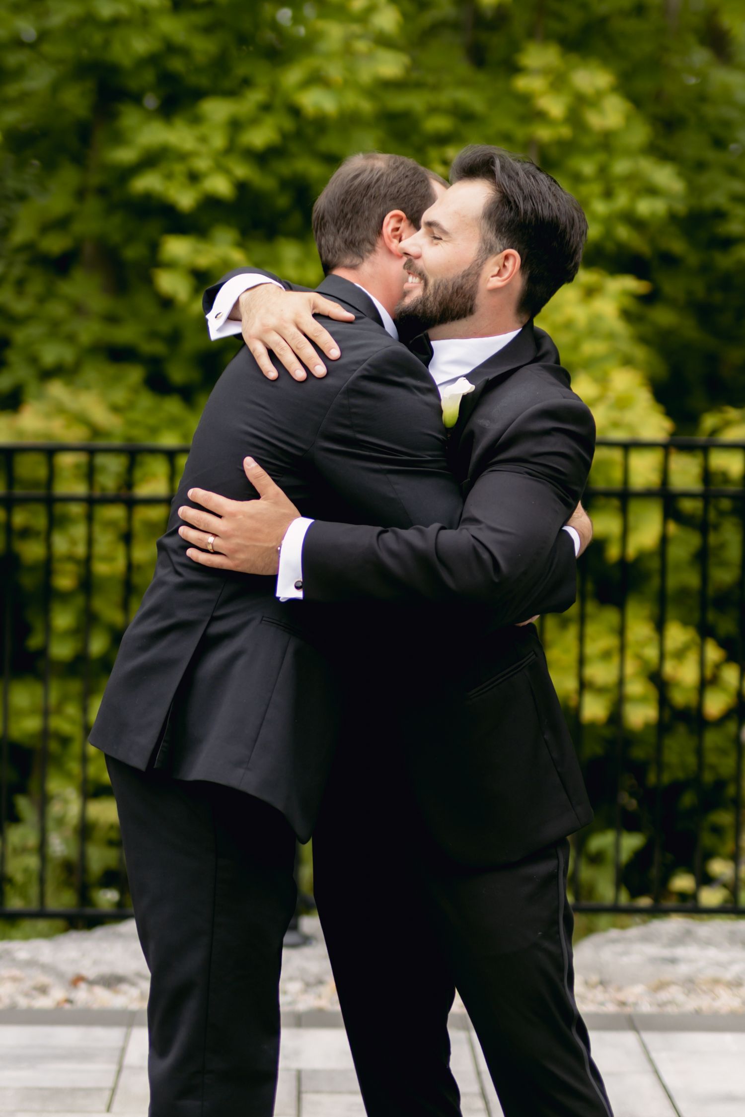 Groom sharing emotional hug with groomsman outdoors before wedding ceremony.
