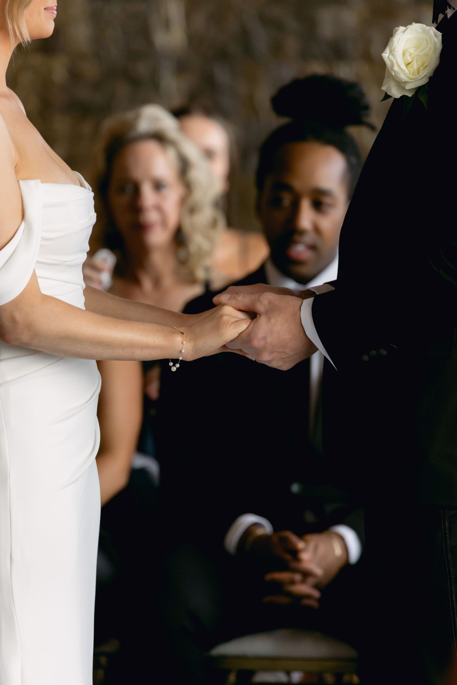 Bride and groom holding hands during wedding ceremony while guests watch attentively in the background.