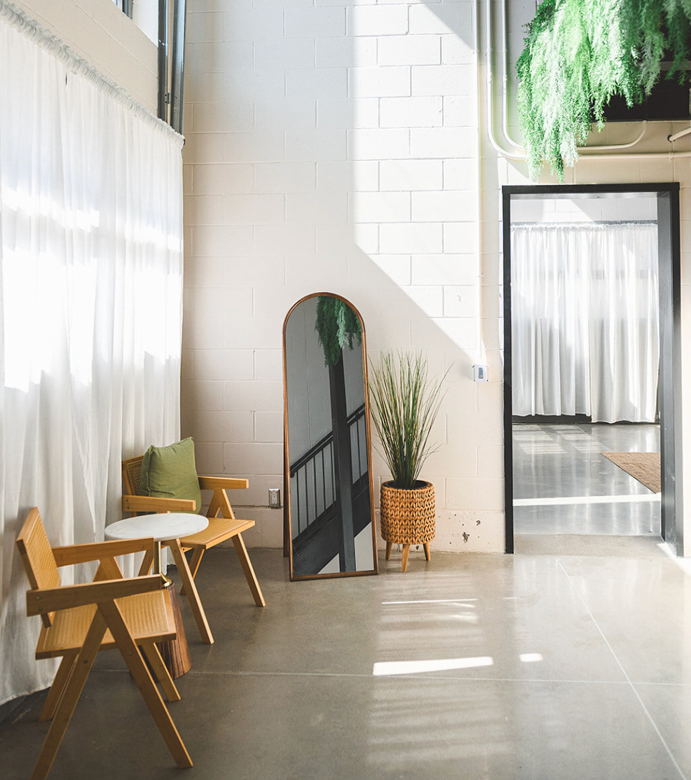 Modern minimalist office space with wooden furniture, white curtains, and natural light streaming through large windows.