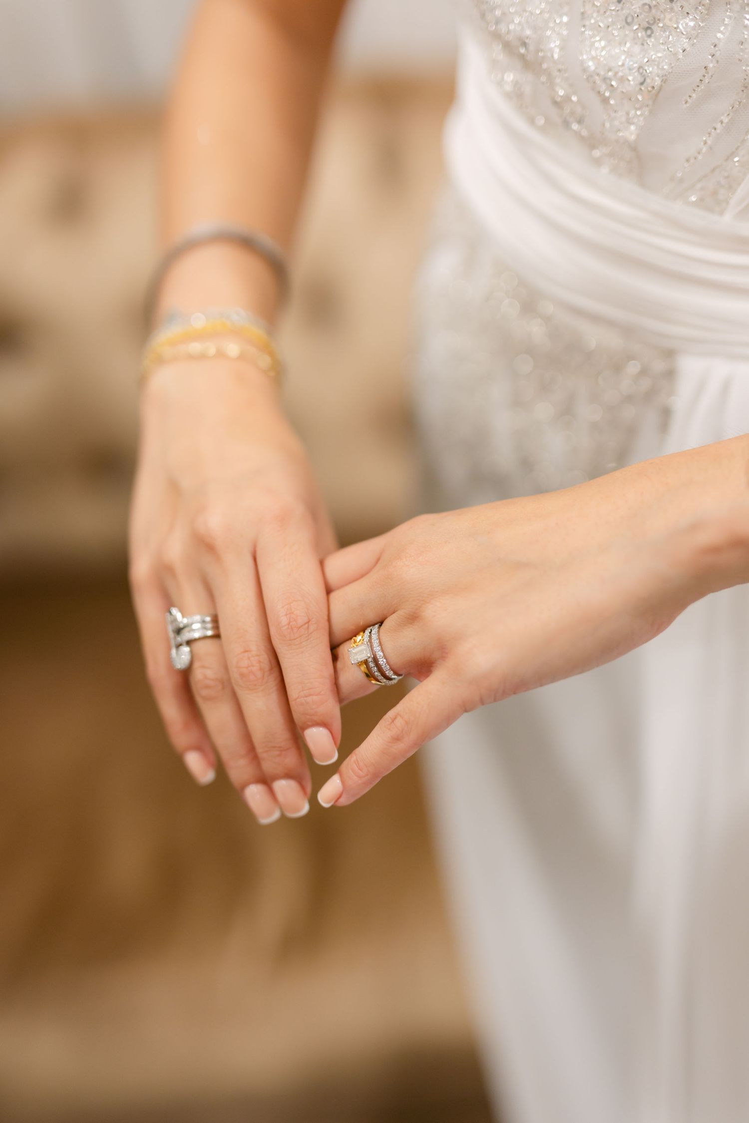 Elegant hands adorned with rings and bracelets against a white dress background.