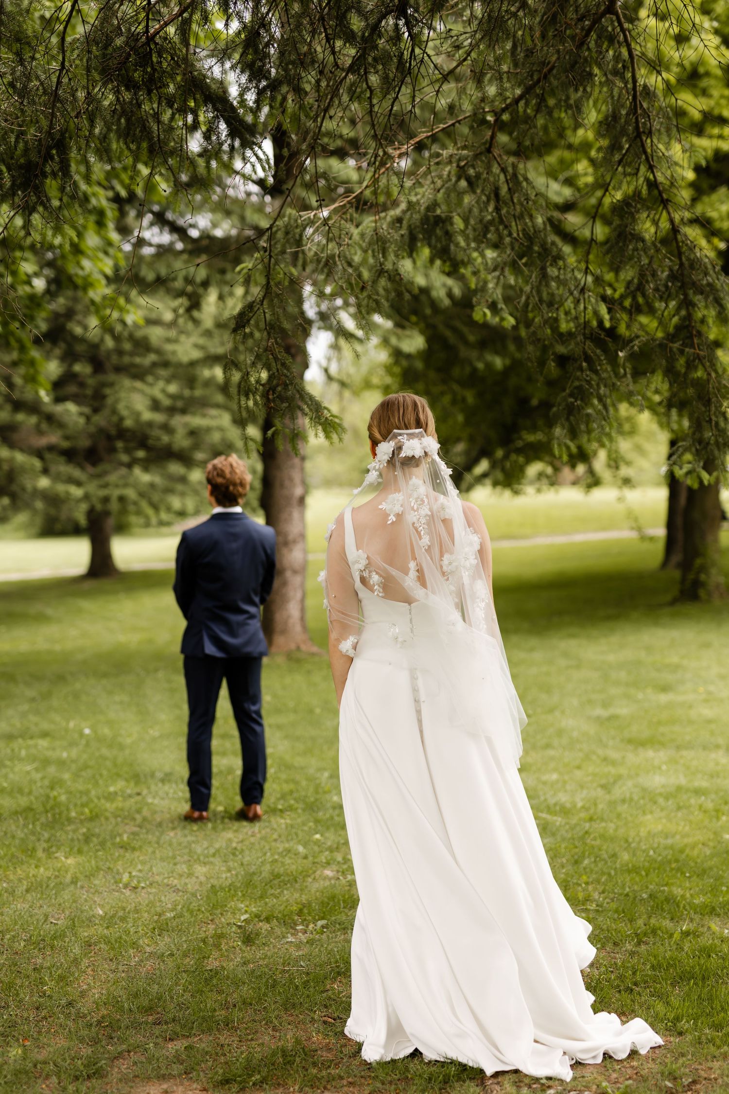 Bride in flowing white dress walks through garden setting with flowing veil.