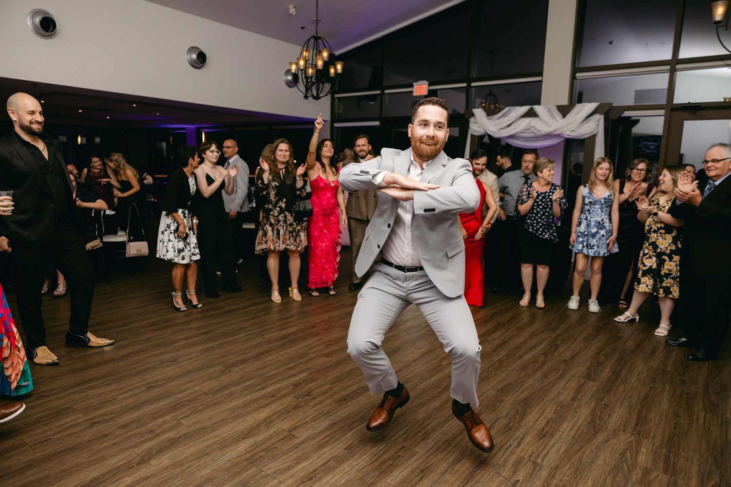 Guests dancing and celebrating with enthusiasm at wedding reception under purple lighting.