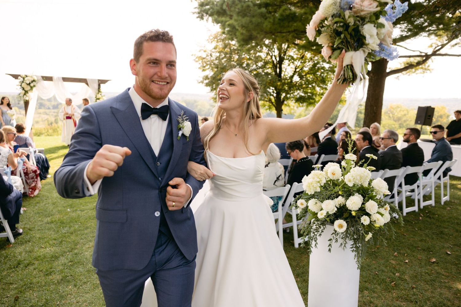 Newlyweds celebrate down the aisle at outdoor ceremony with white floral decorations.
