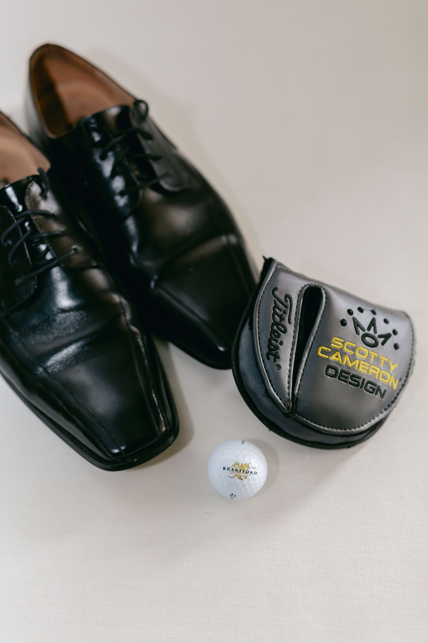Black formal dress shoes and golf accessories arranged on white background.