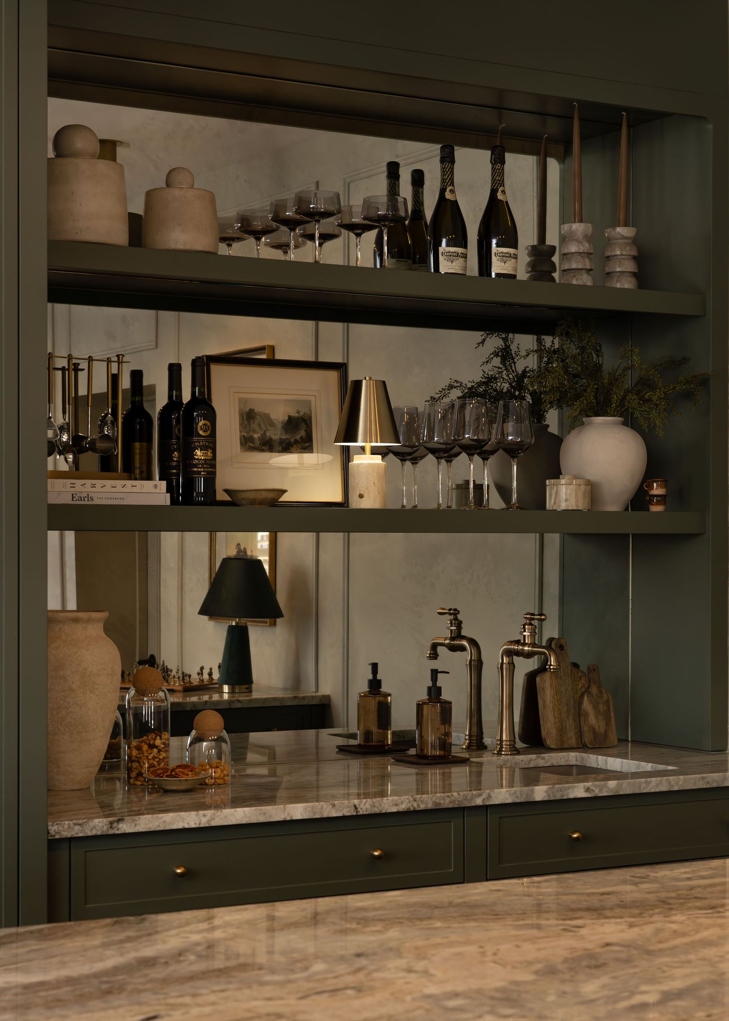 Modern bar interior with marble countertops and dark shelving displaying bottles and glassware.