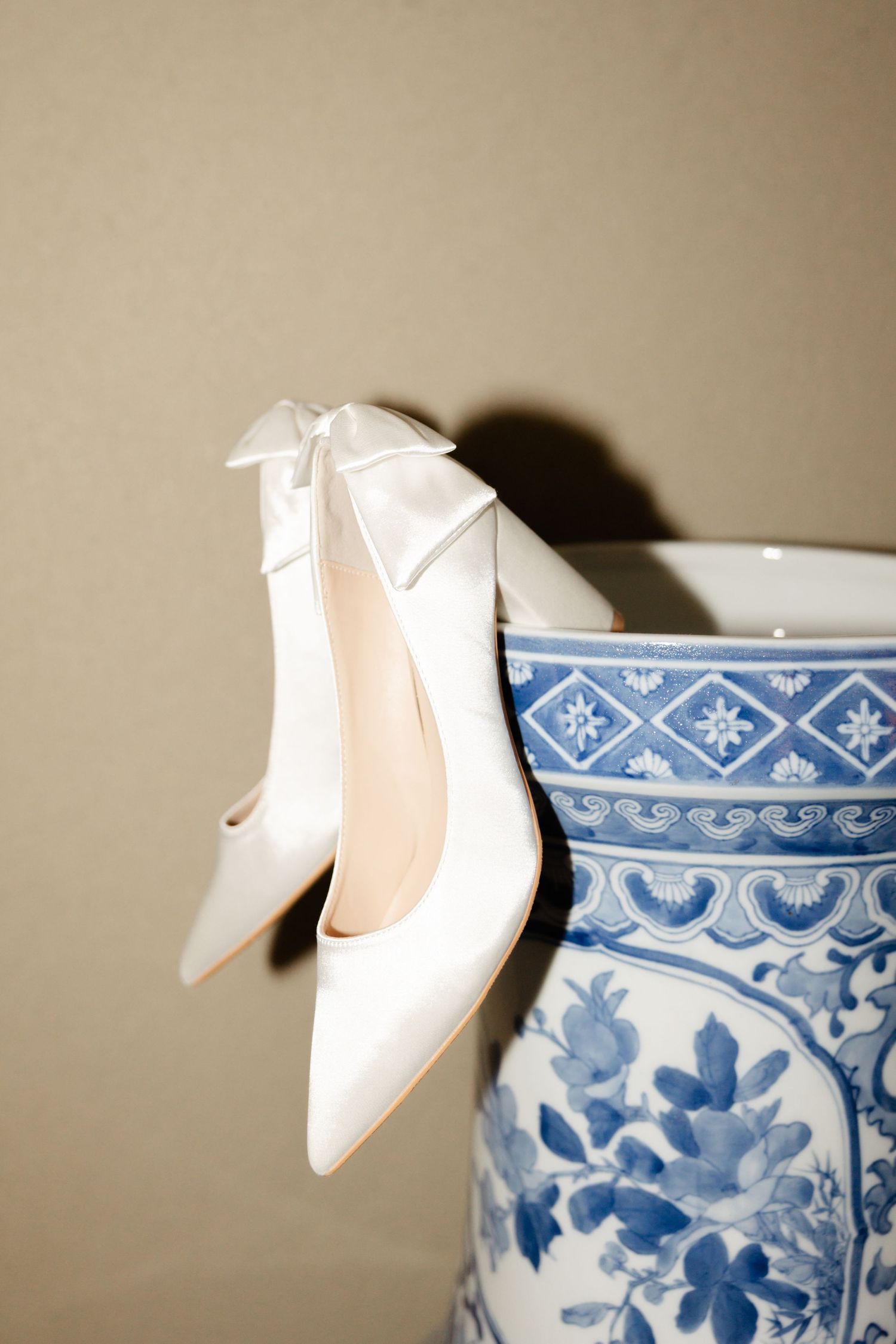 White bridal heels with bows positioned next to a blue and white porcelain vase.