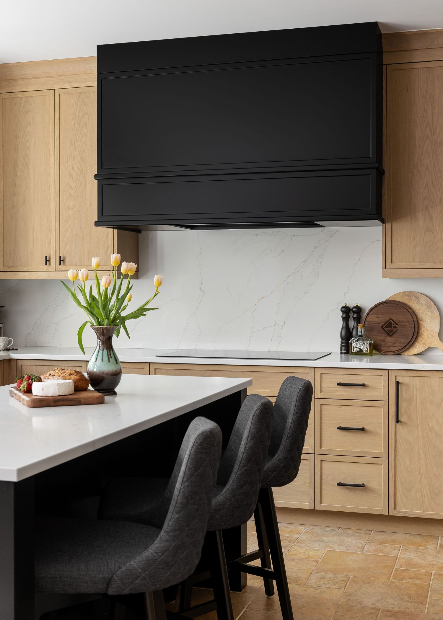 Modern kitchen island with black upholstered chairs and light wood cabinetry.