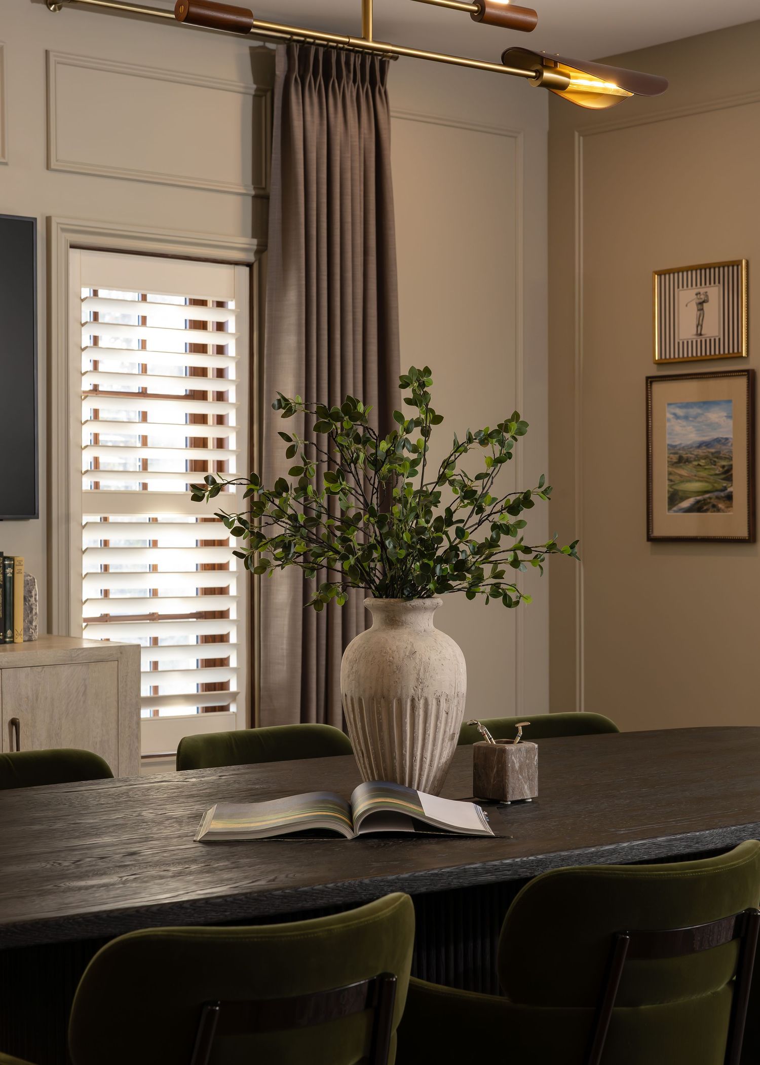 Dining room featuring dark green chairs, white ceramic vase, and natural light from shuttered windows.