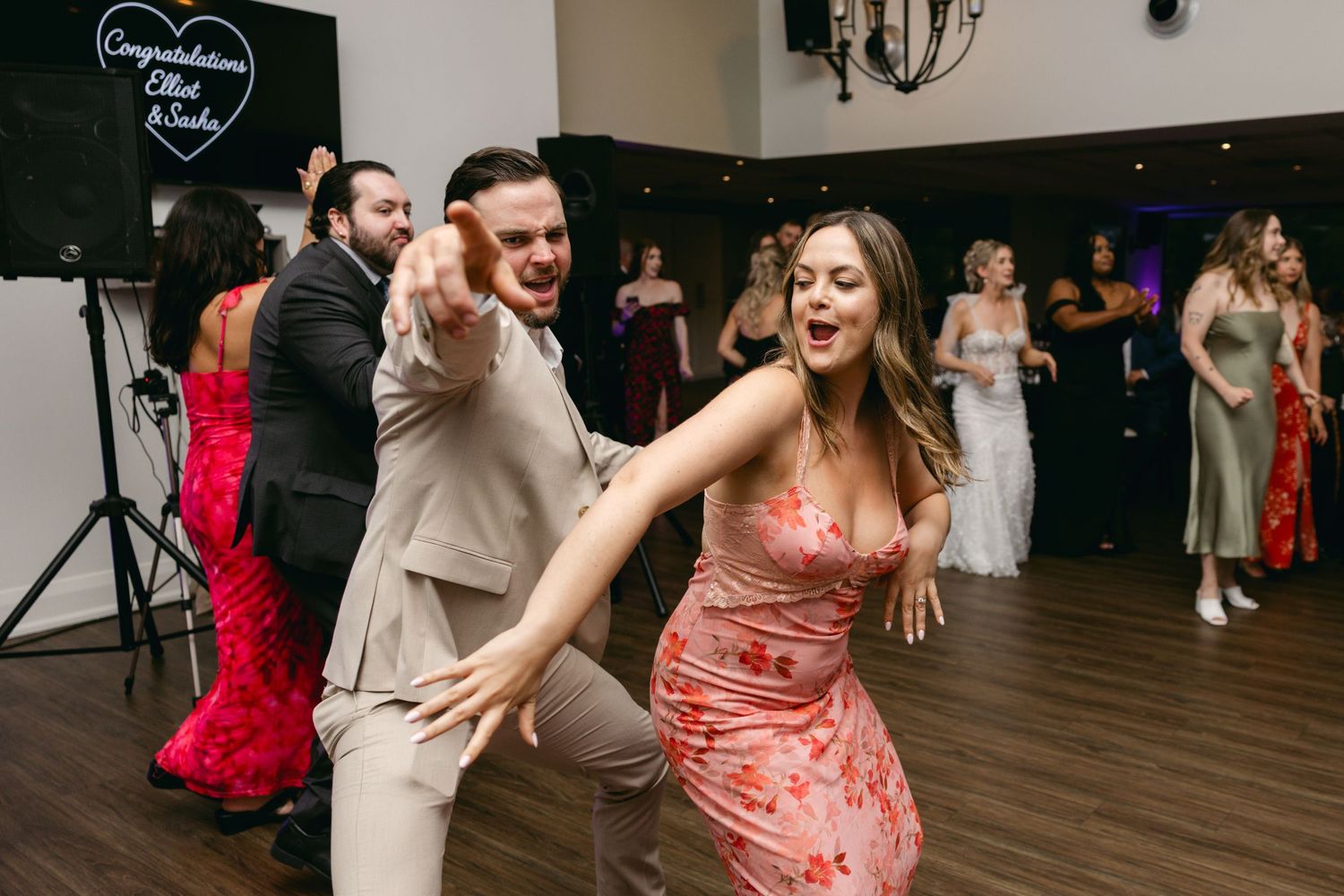 Wedding reception dance floor filled with guests enjoying upbeat celebration under chandeliers.