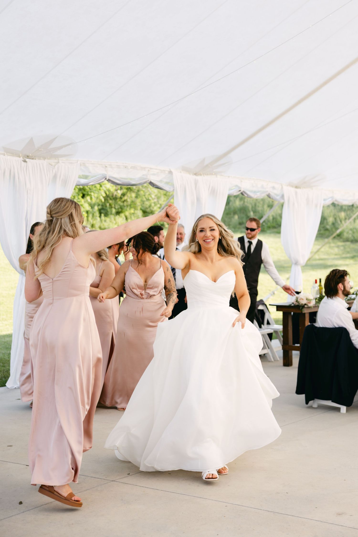 Wedding celebration with guests in pink dresses dancing under white tent.