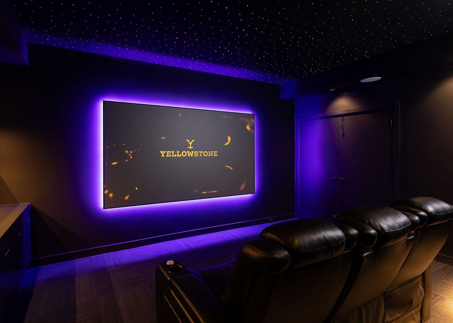 Modern home theater with purple LED accent lighting and black leather seating creates a luxurious viewing environment.