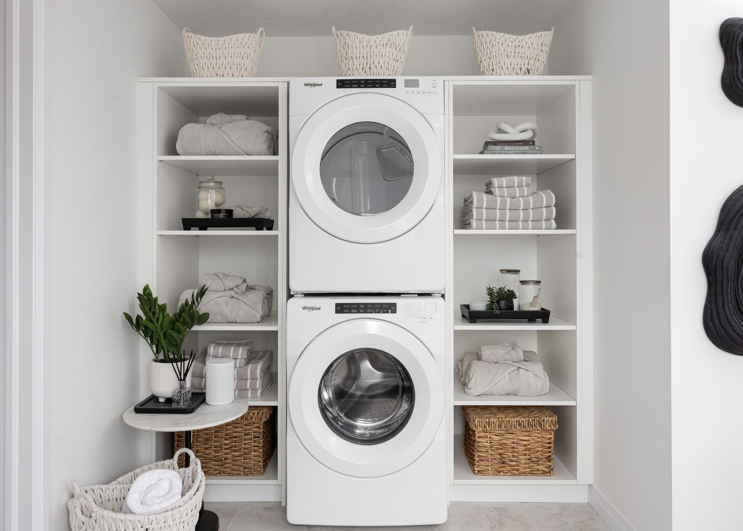 Modern white laundry room with stacked washer and dryer flanked by built-in storage shelves.