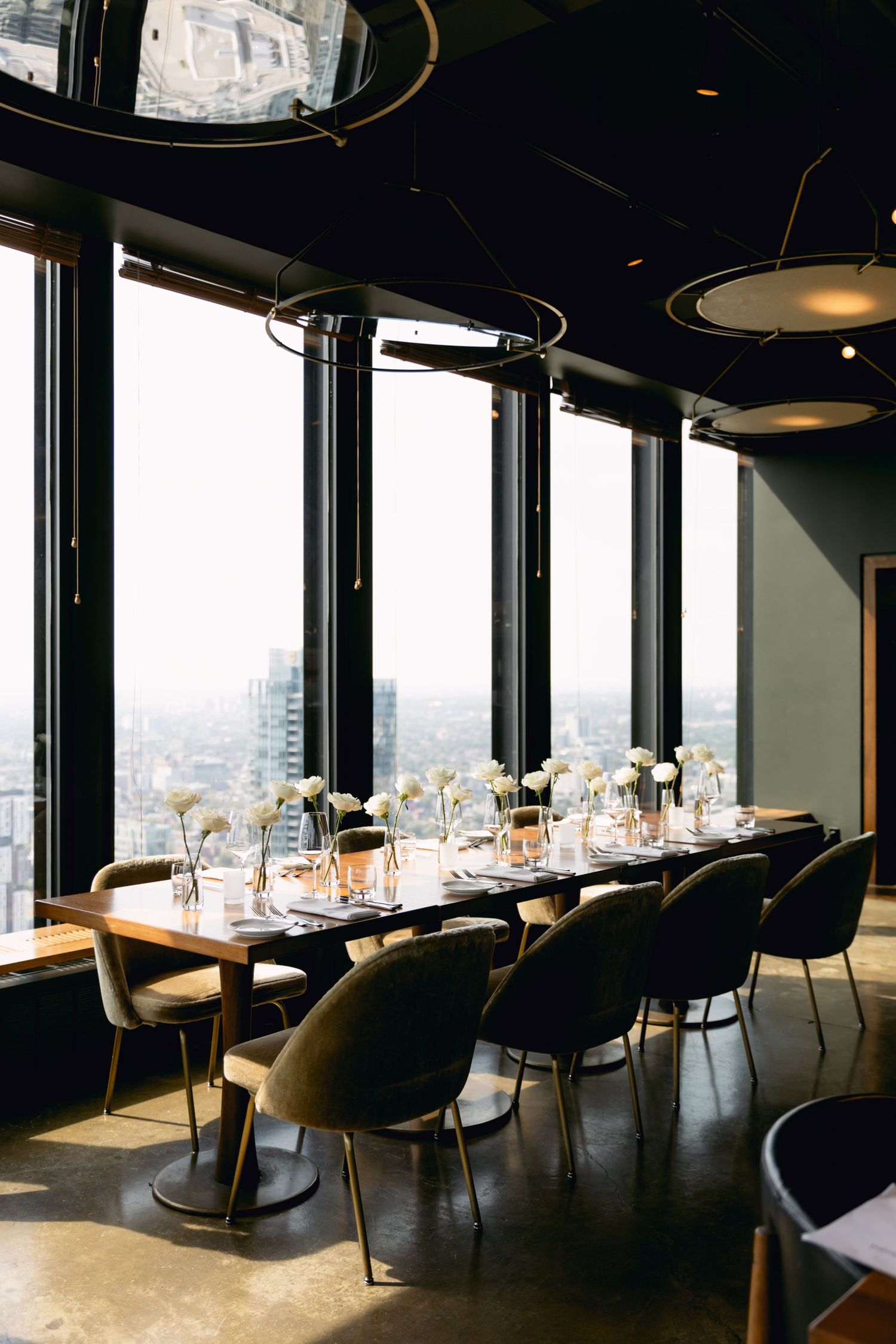 Elegant high-rise restaurant dining table set for a wedding reception with city views through floor-to-ceiling windows.