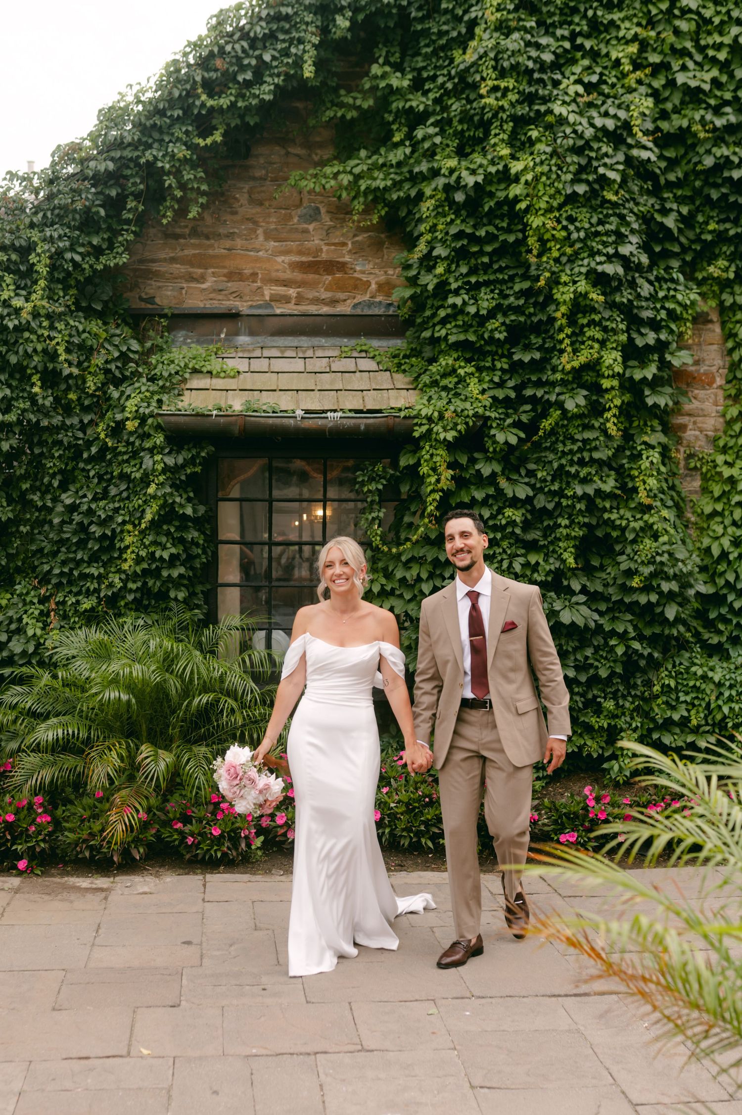 Elegant wedding portraits in front of stone building with climbing ivy and tropical plants.