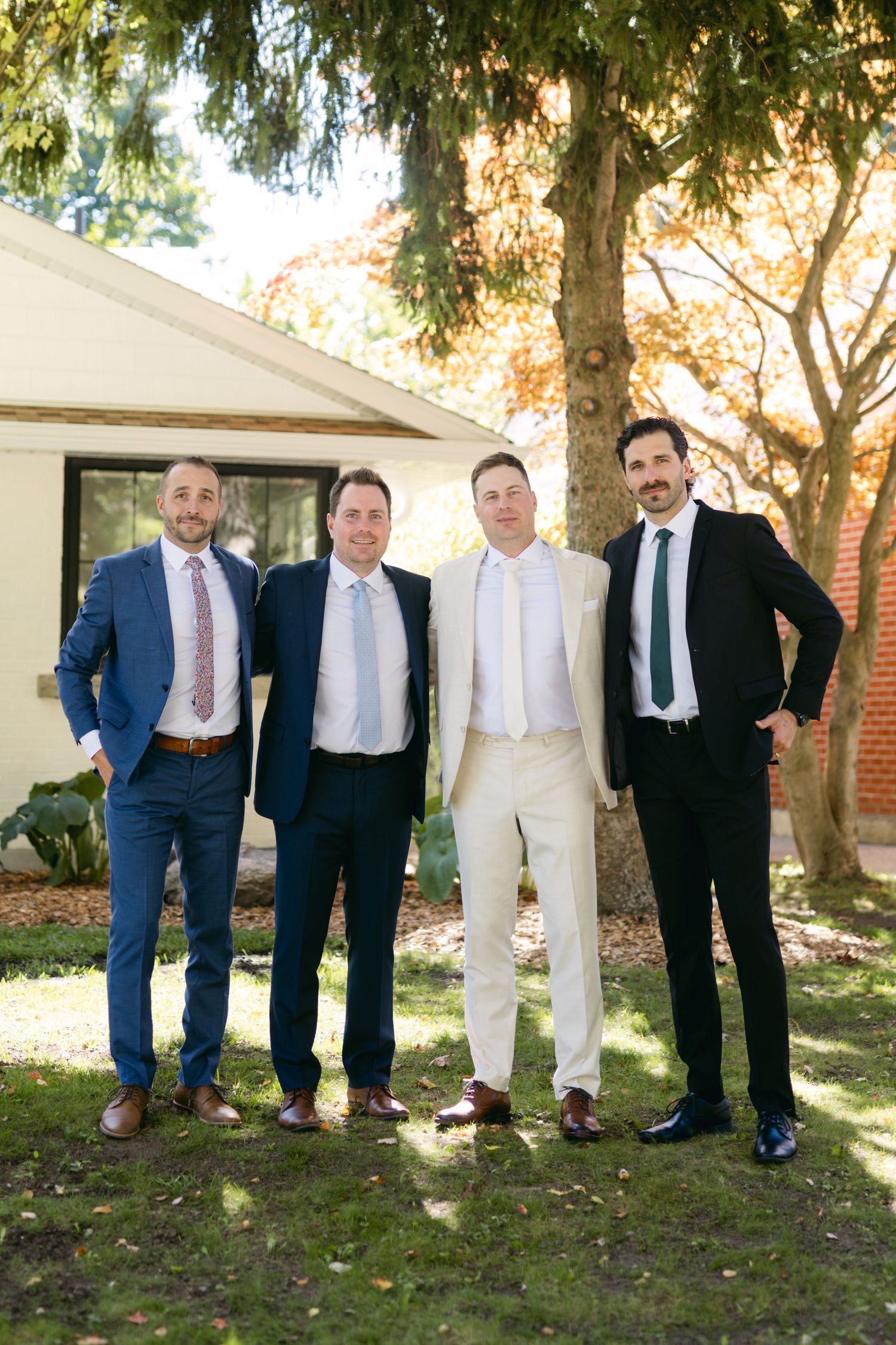 A group poses together outdoors wearing formal suits in dark and light colors.