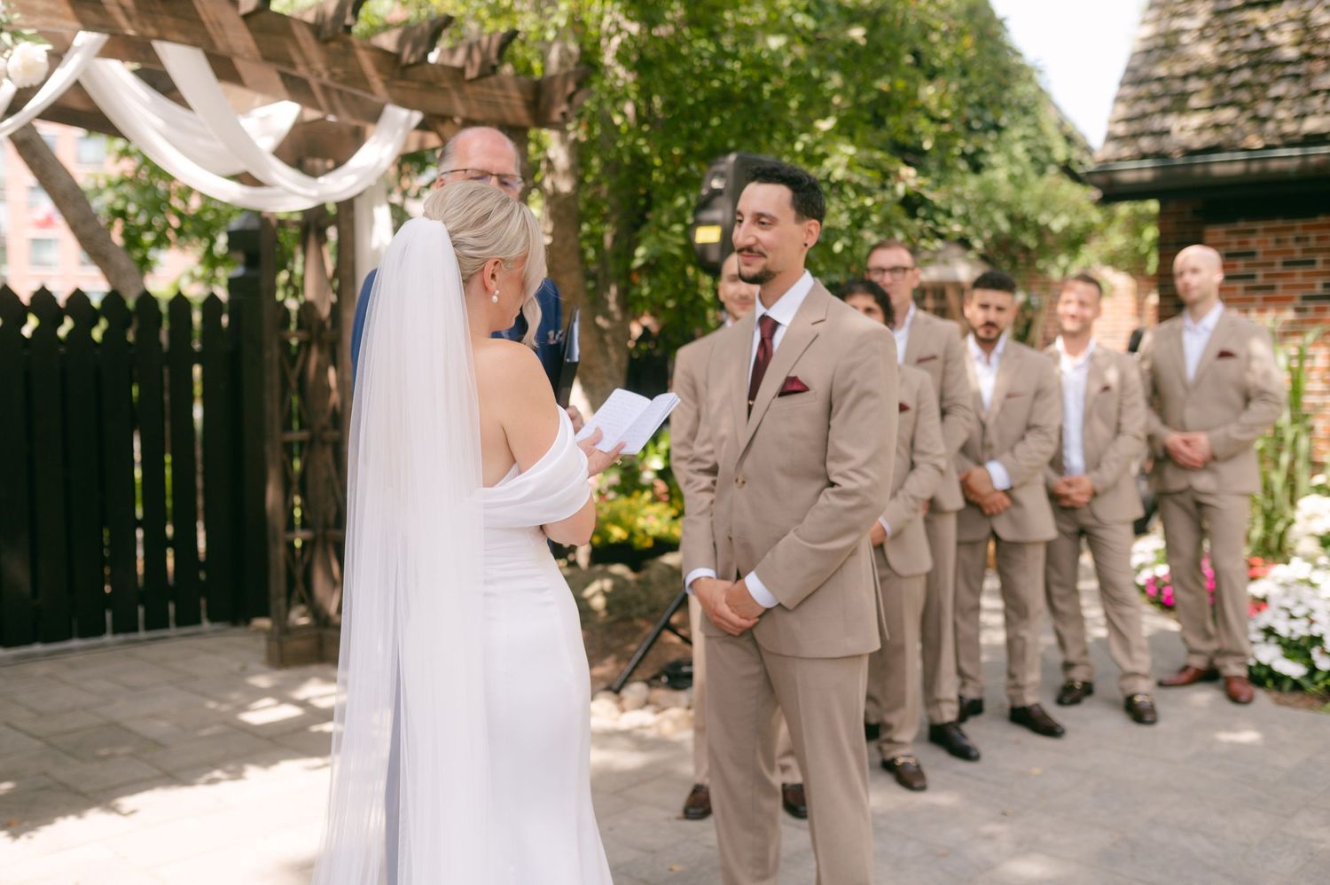 Wedding party members gather on a stone patio surrounded by lush greenery.