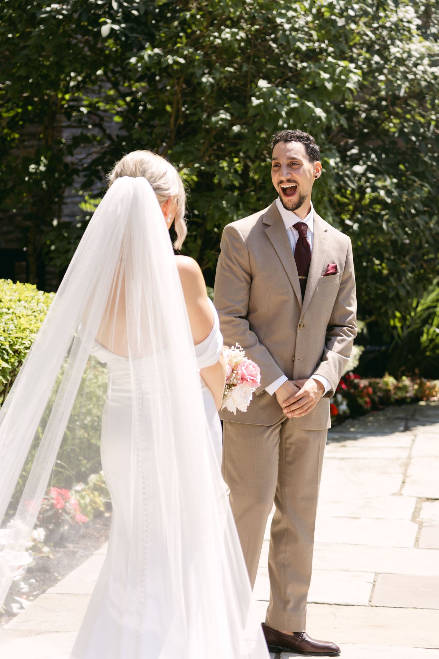 First look wedding moment captured in garden setting with stone architecture.