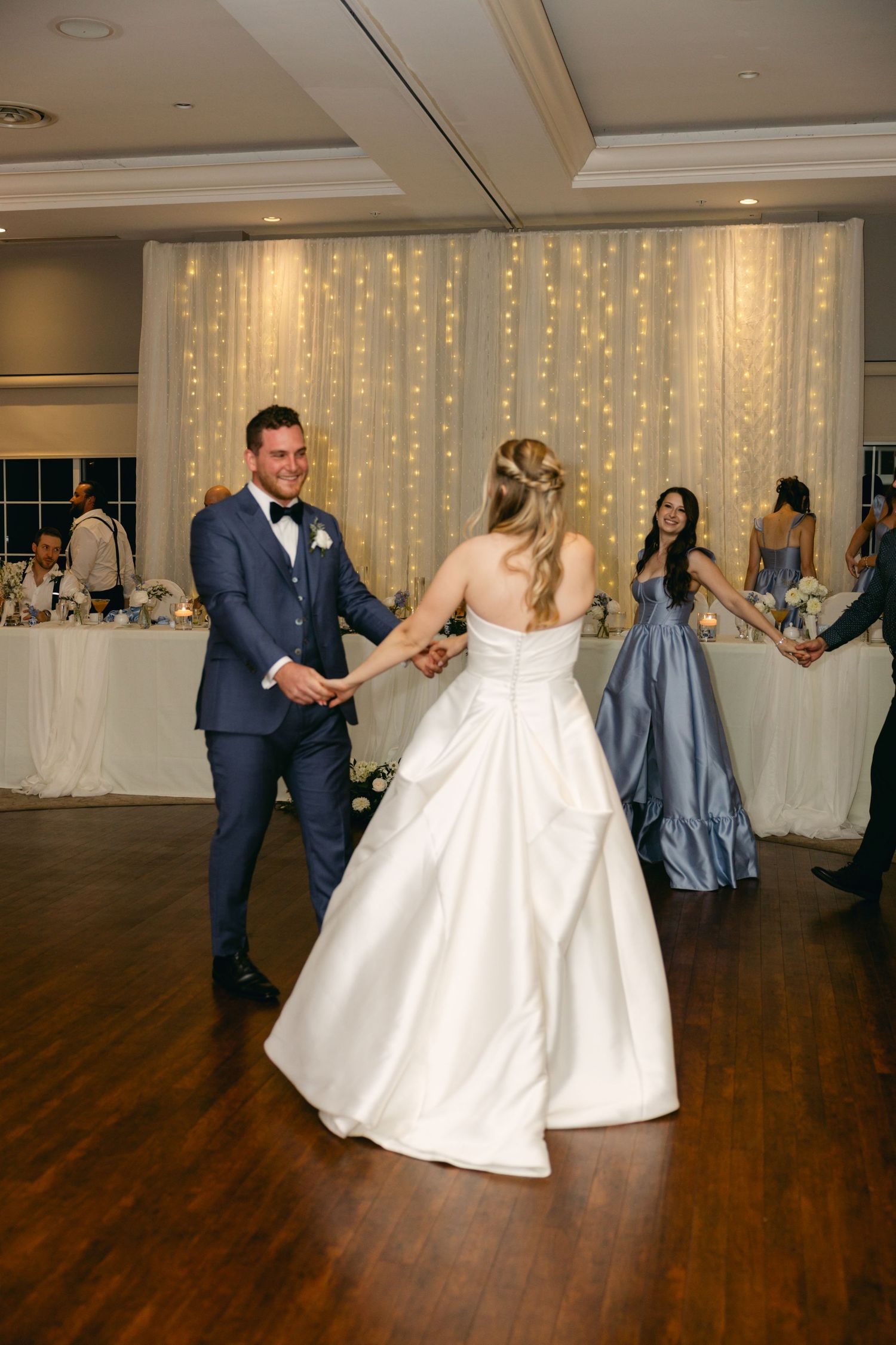 Joyful dancing at wedding reception with white gown twirling on wooden dance floor.