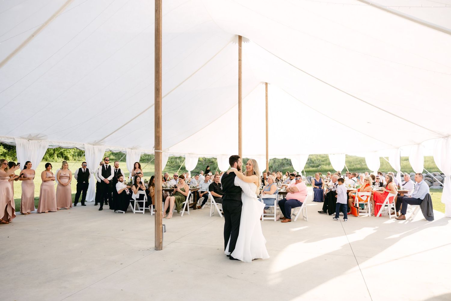Wedding party dancing and celebrating under a spacious white tent pavilion.