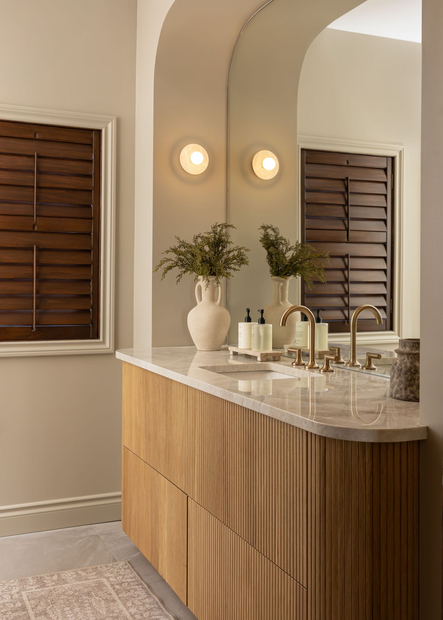 Modern bathroom vanity with wooden cabinets, marble countertop, and decorative vase with greenery.