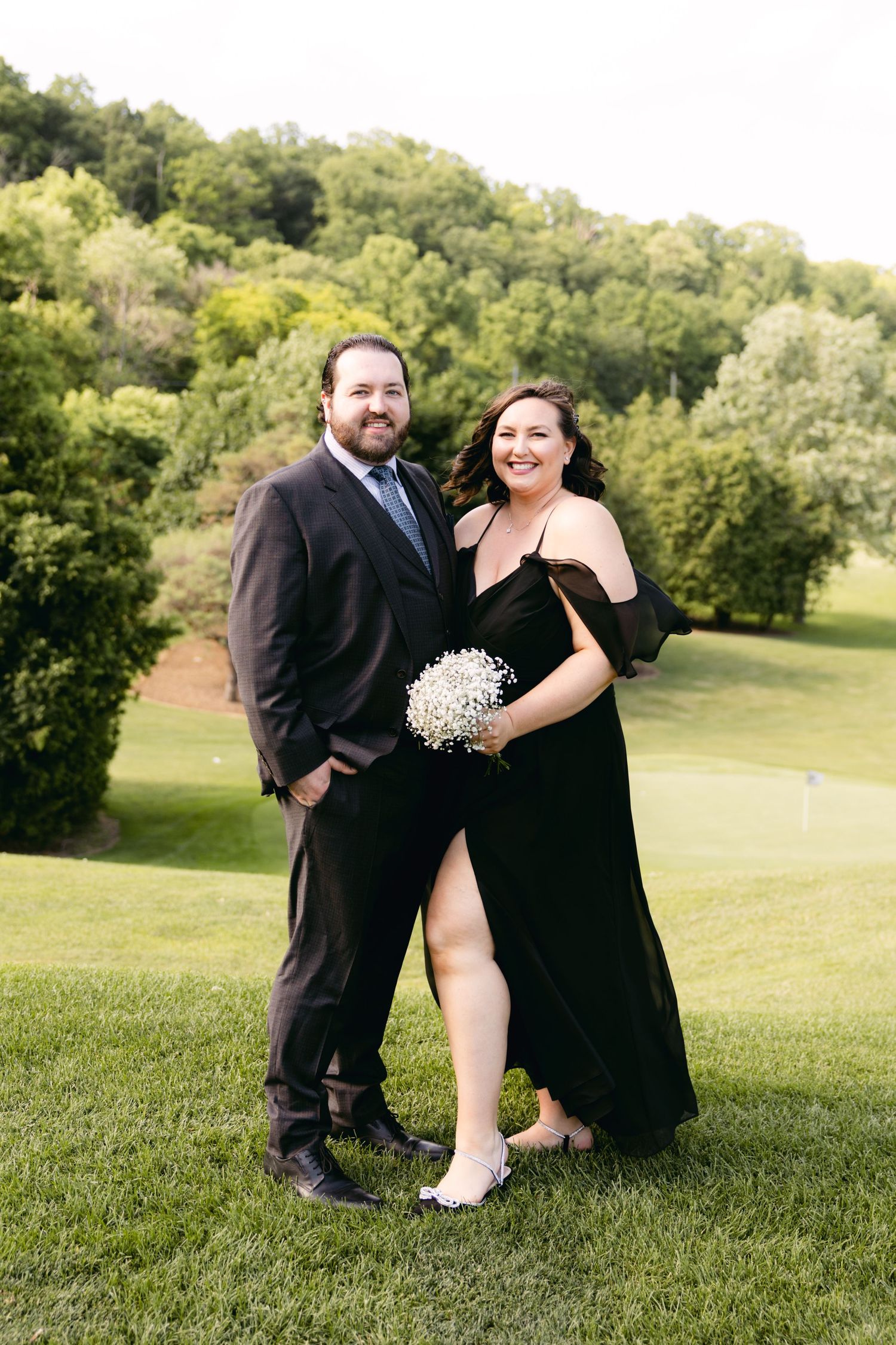 Wedding party members in black formal attire pose casually on a sunny golf course.