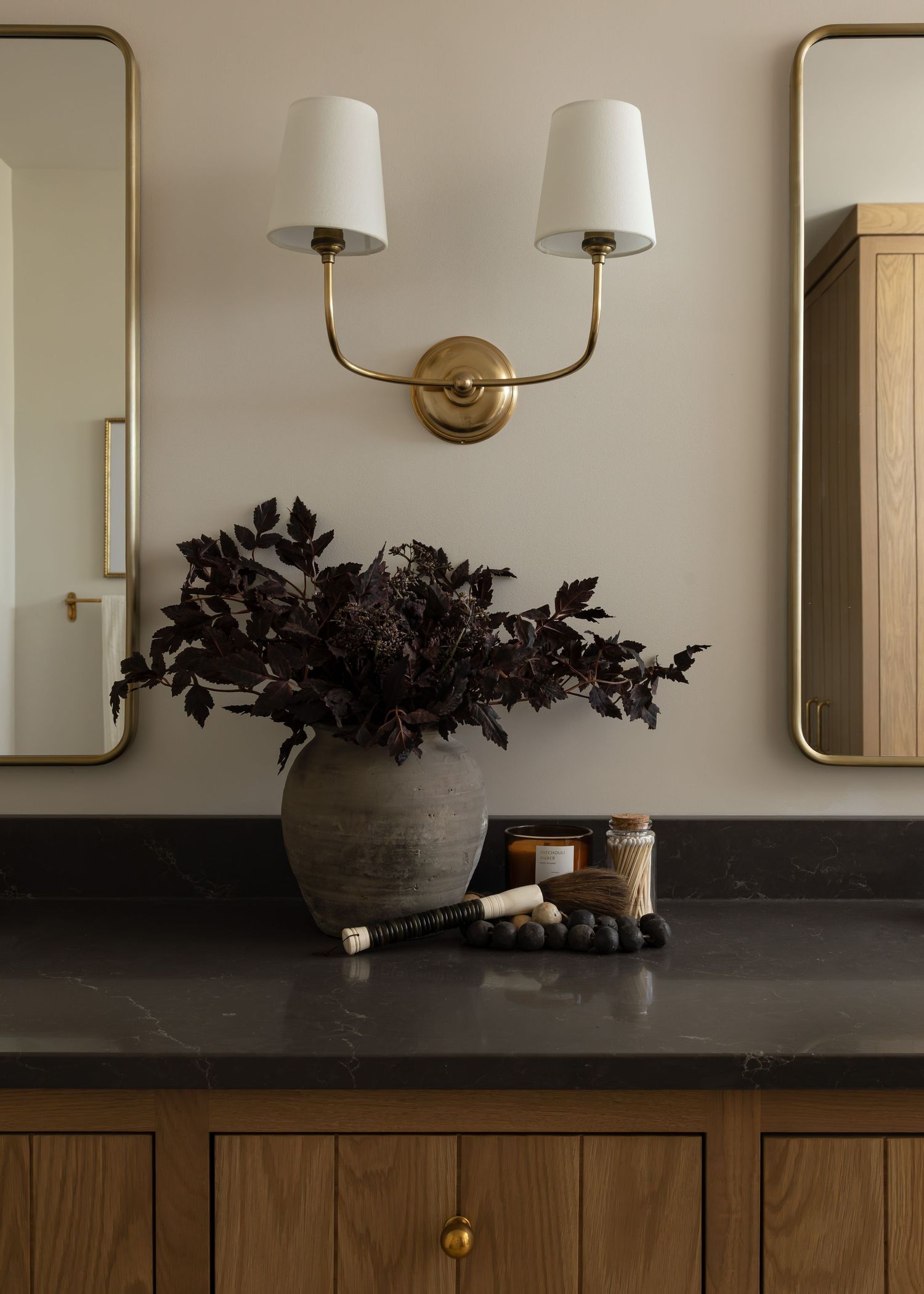 Contemporary vanity with black countertop, brass sconces, and wooden accents in a neutral bathroom.
