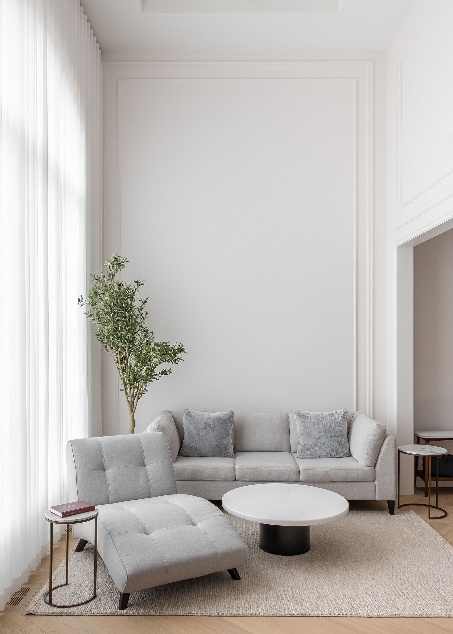 Minimalist living room with gray seating, round table, and large windows.