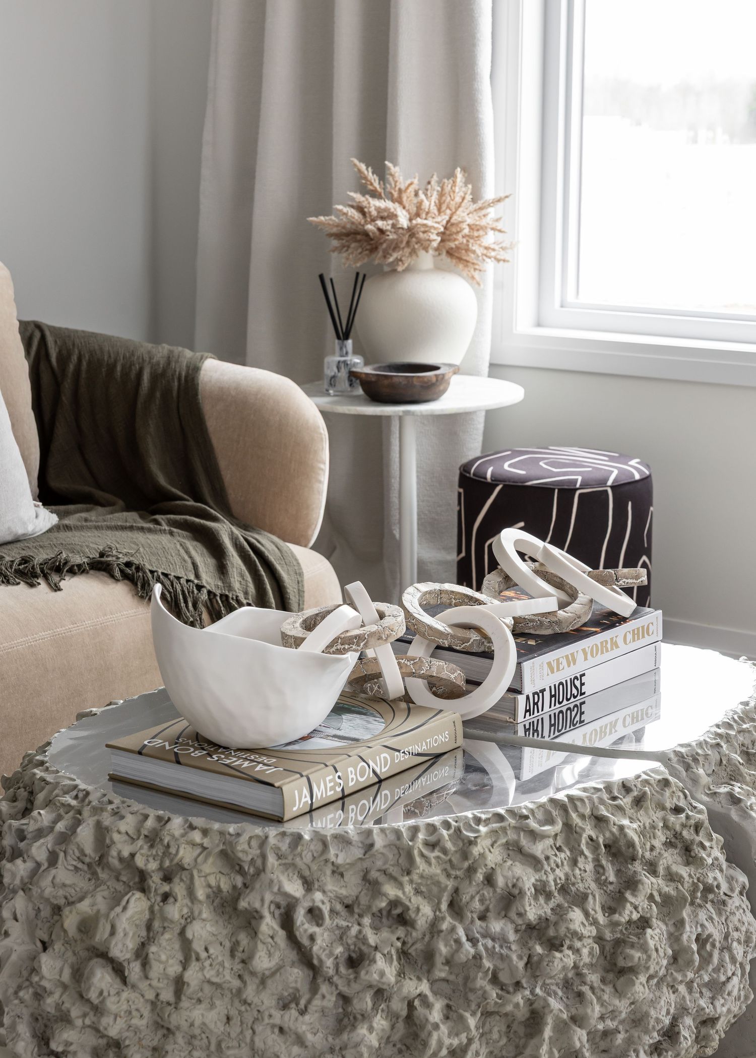 Cozy living room corner with beige sofa, textured ottoman, and dried pampas grass arrangement on side table.
