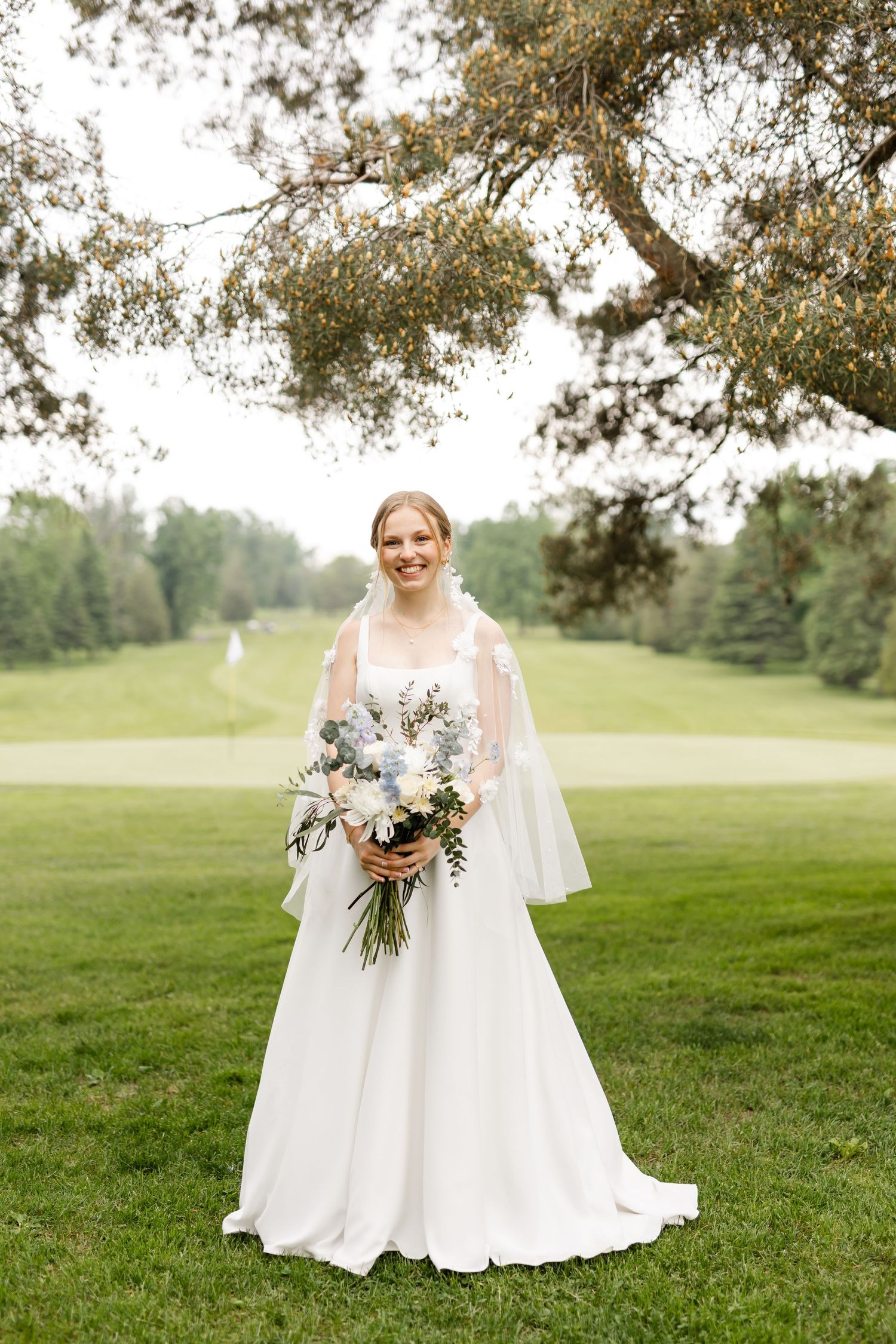 Classic bridal portrait on golf course with flowing white dress and floral bouquet.