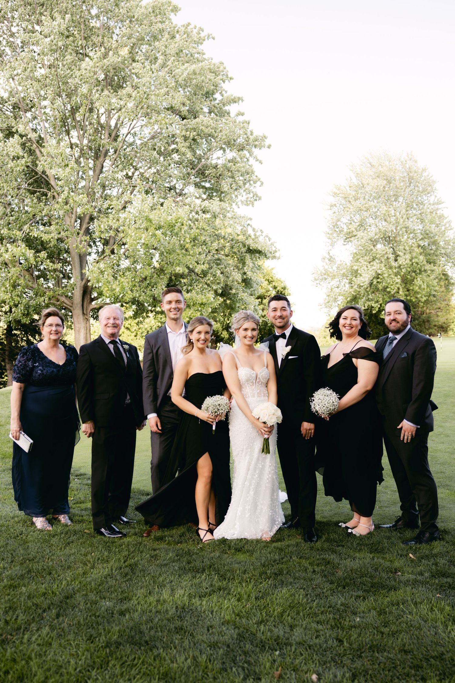 Wedding party poses playfully on grassy hill for candid group photos in formal attire.