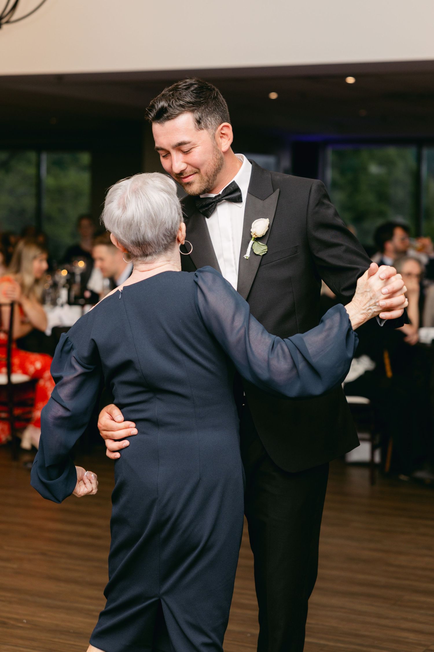 Wedding guests dancing on wooden floor during evening reception celebration.