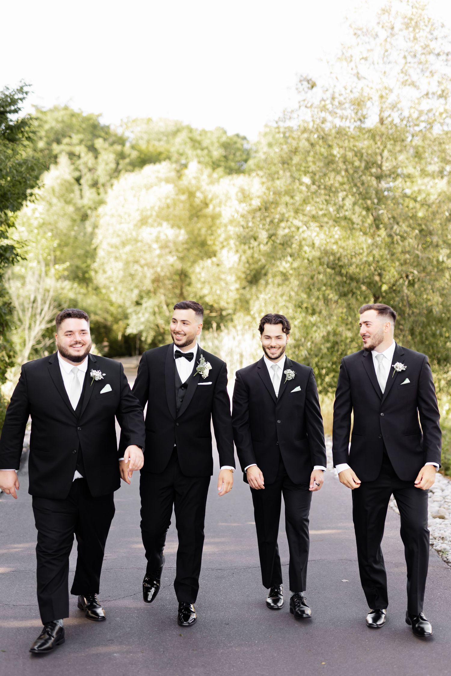 Groomsmen in black suits walking in formation on outdoor path during wedding photoshoot.