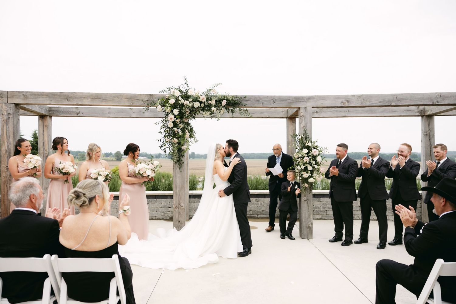 Panoramic view of an outdoor wedding ceremony with guests seated under a decorated wooden structure.
