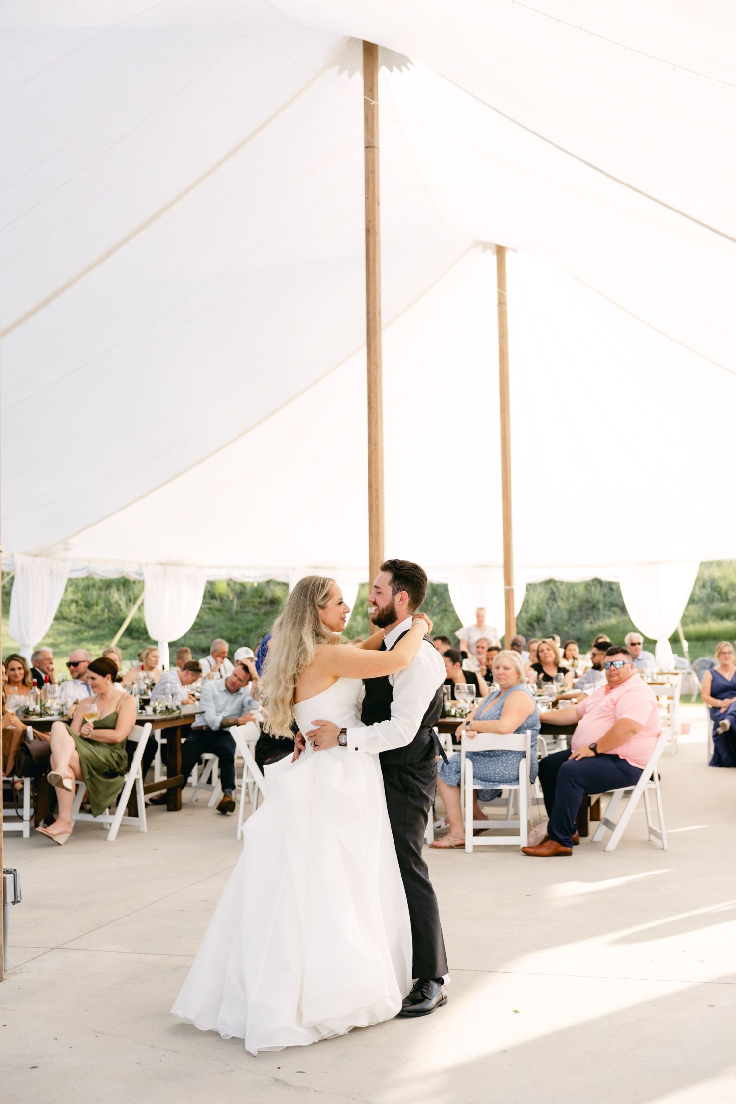 Wedding guests celebrate under an elegant white tent during an outdoor reception.