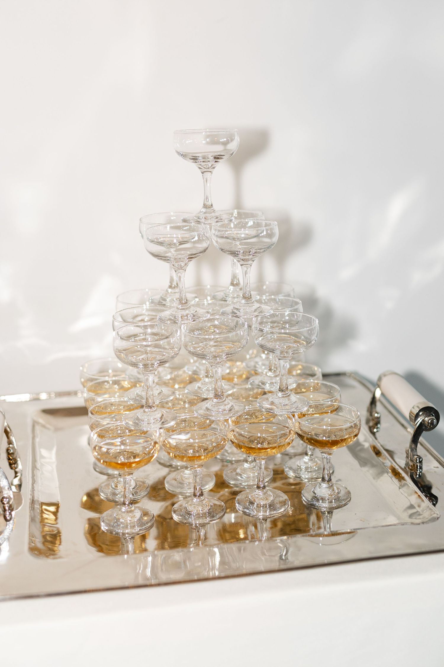 Elegant champagne tower setup with coupe glasses arranged on a mirrored tray for a special event.
