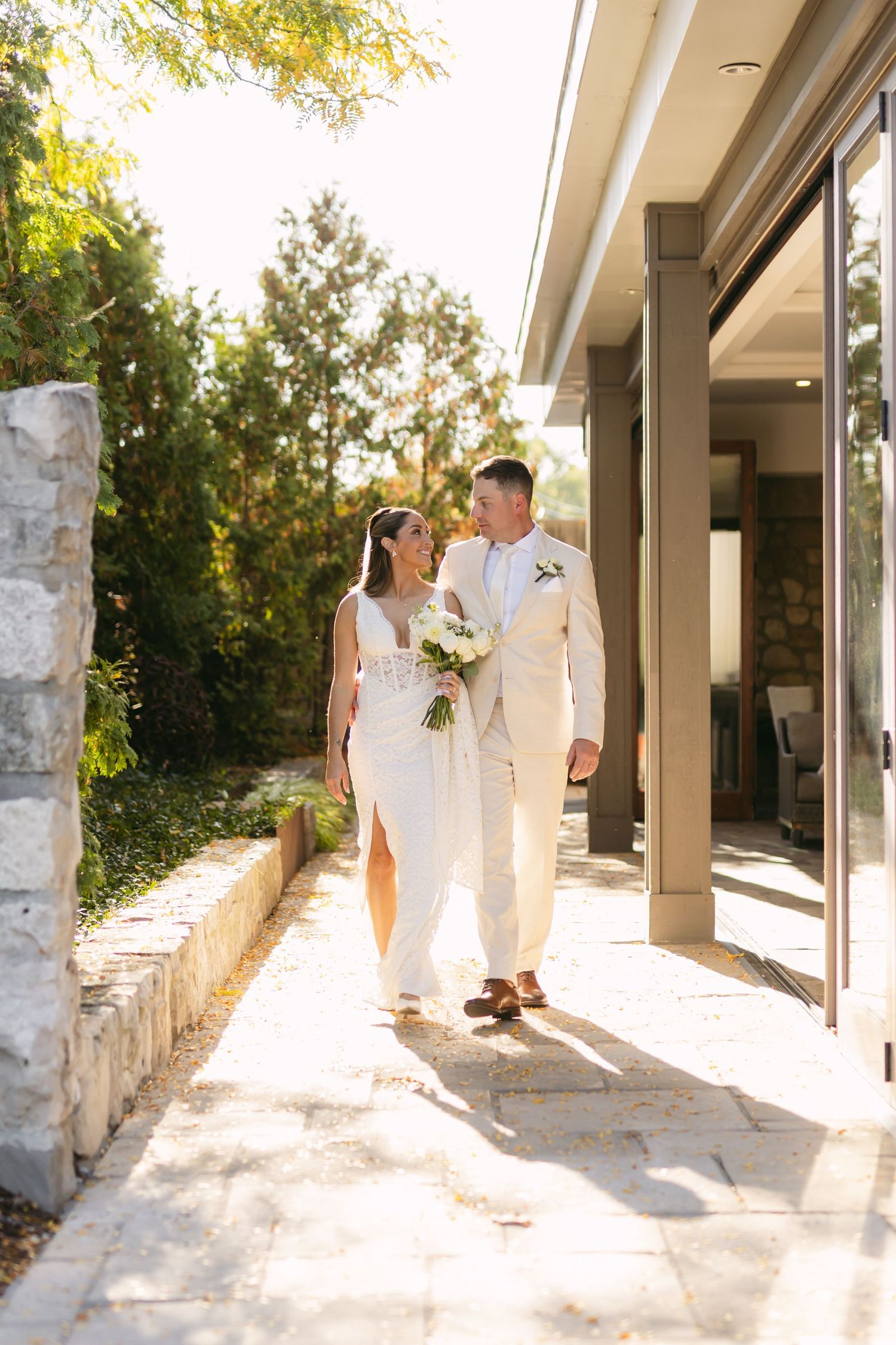 Wedding couple poses in sunlit corridor with stone columns and modern architecture.