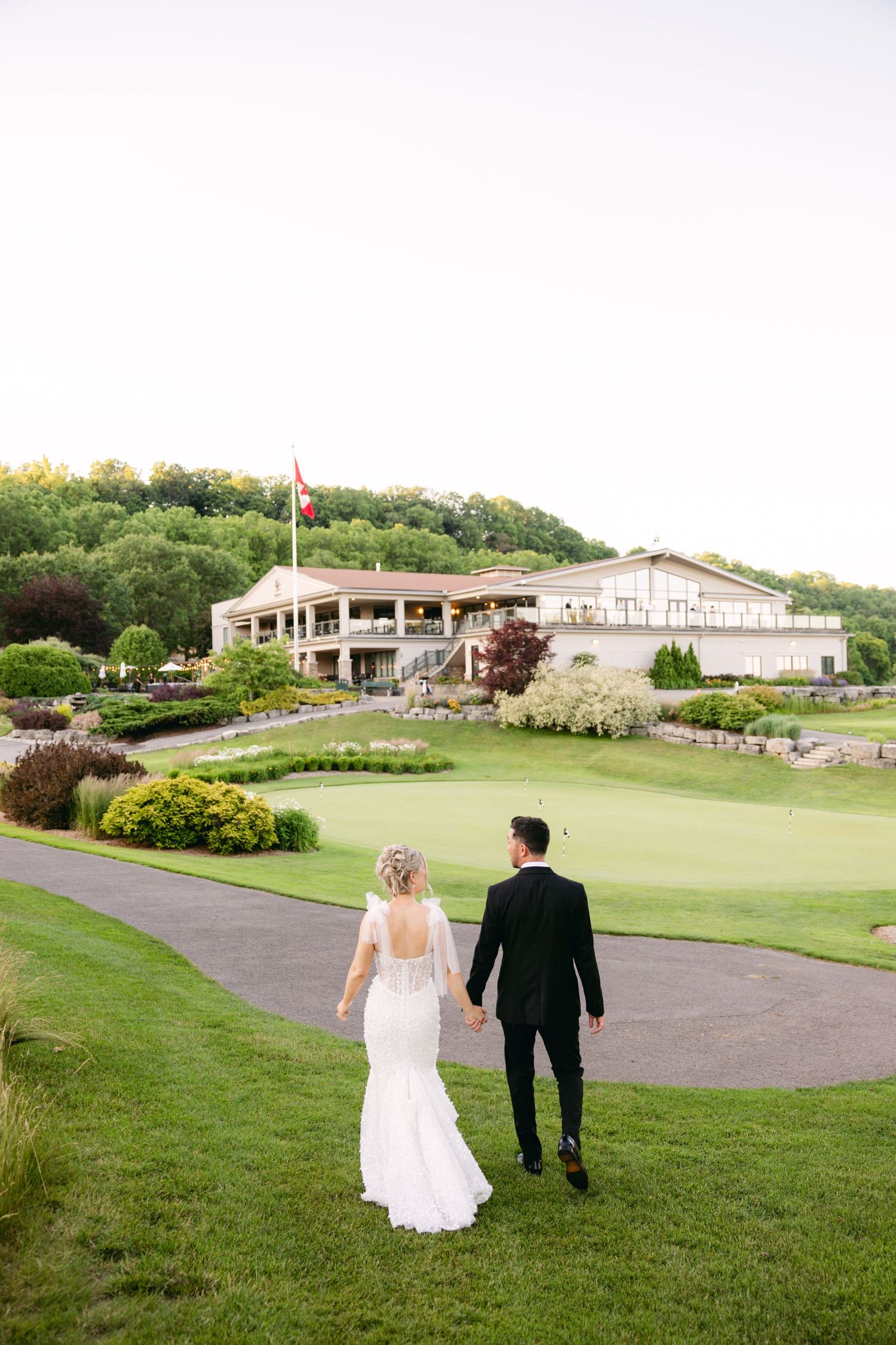 Couple walking on manicured golf course grounds with clubhouse and flag visible in background.