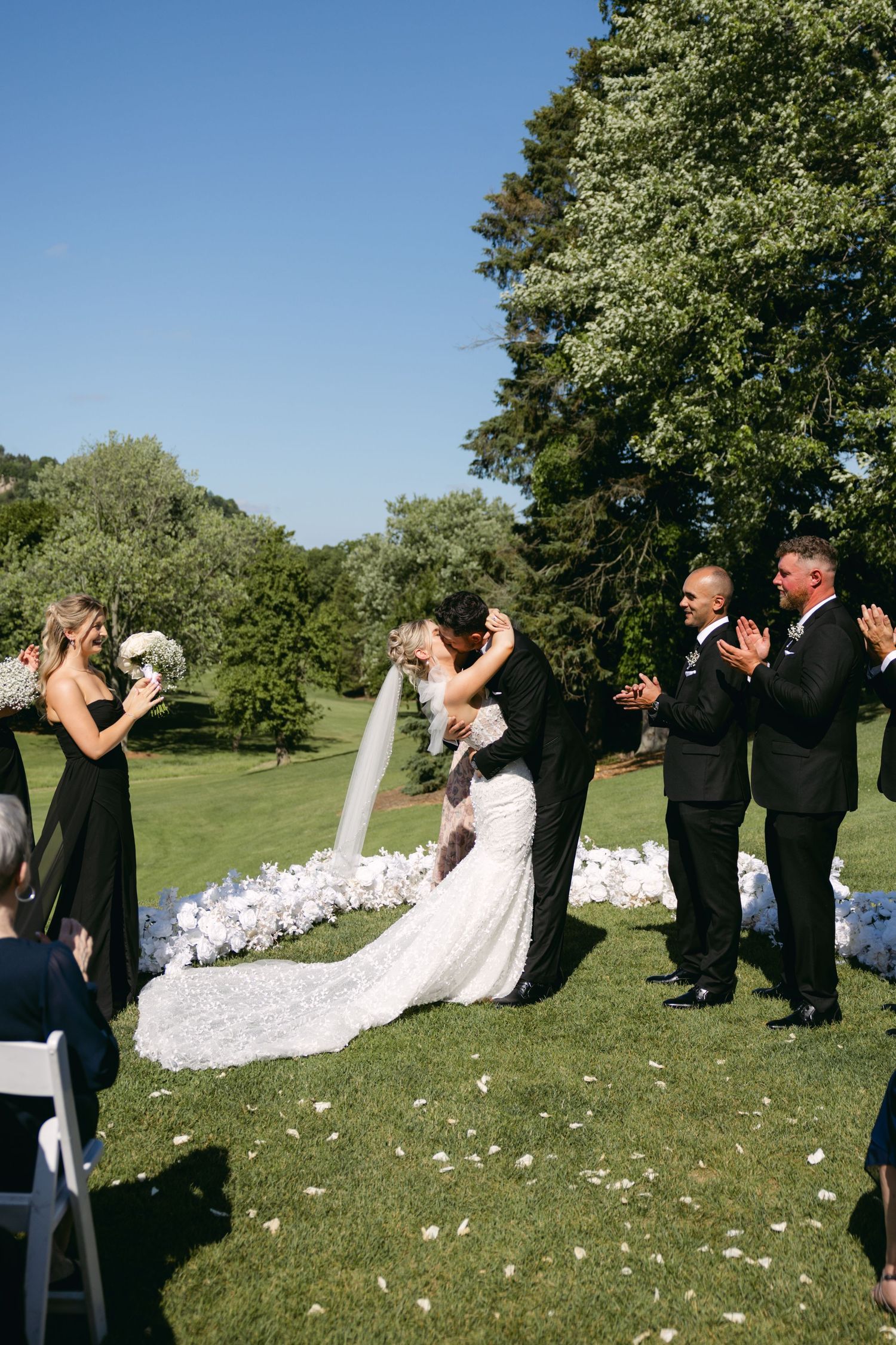 Wedding ceremony taking place on a grassy hill with white flower petals scattered along the aisle.