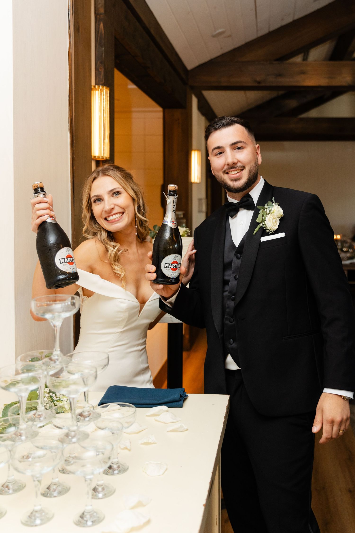Newlyweds pouring champagne into a tower of coupe glasses at their wedding reception.